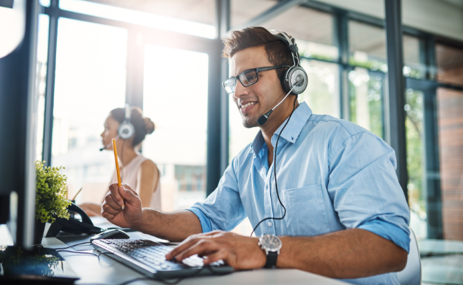 A man with headphones and a headset is focused on his work at a computer.