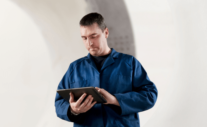A man in a blue work uniform uses a tablet.