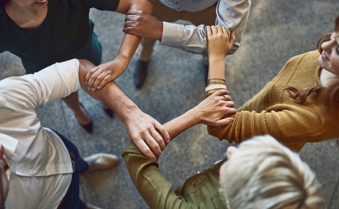 A group of people standing in a circle, linking hands together as a symbol of teamwork and unity.