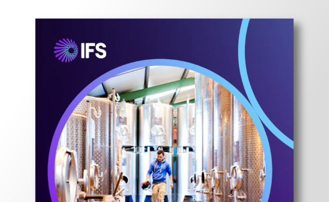 A man walking between large stainless steel tanks or vats.