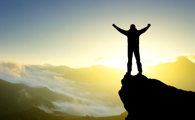 Person celebrating on a mountain peak at sunrise