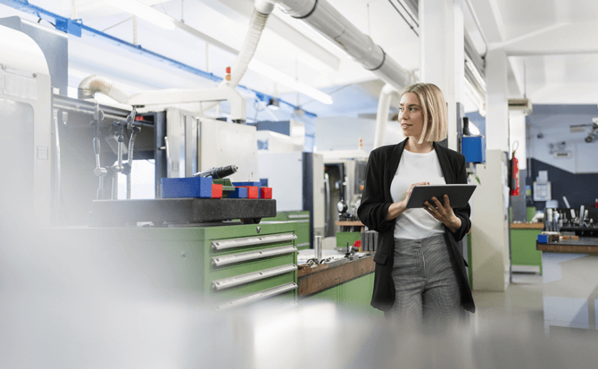 Una professionista in un ambiente industriale moderno utilizza un tablet con CMMS software per gestire macchinari e attrezzature, evidenziando l'efficienza della manutenzione digitale.