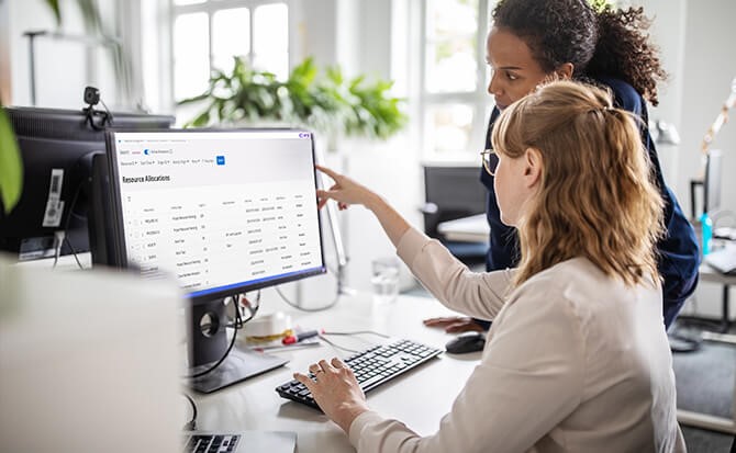 Two professionals using Sustainability Solutions to analyze resource allocation data on a computer screen in a modern office setting.