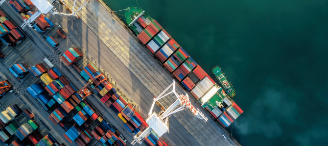 Aerial view of a shipping port illustrating global supply chain resilience, with cargo ships docked alongside rows of multicolored containers being loaded and unloaded by cranes. The image reflects efficient maritime logistics, import-export operations, and the importance of robust supply chain infrastructure.