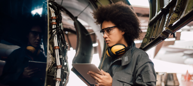 A defense industry technician using a tablet for aircraft inspection, illustrating digital transformation in the defense industry