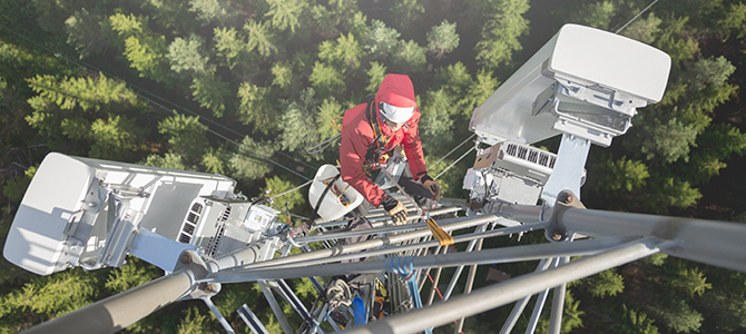 Telecommunication manual high worker engineer installing new 3g 4g LTE antenna on tall mobile base station (communication tower) in the middle of european forest, high angle of view. Working at height. Telecommunication masts and towers are typically tall structures designed to support antennas for telecommunications and broadcasting. Drone point of view.