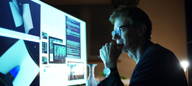 Software engineer wearing glasses studies 3-D models and code on a glowing widescreen monitor at night, illustrating hands-on interaction with Agentic AI development tools.