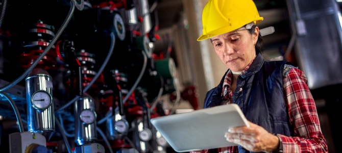 Engineer using predictive maintenance software on a tablet to analyze real-time equipment data in an industrial facility.