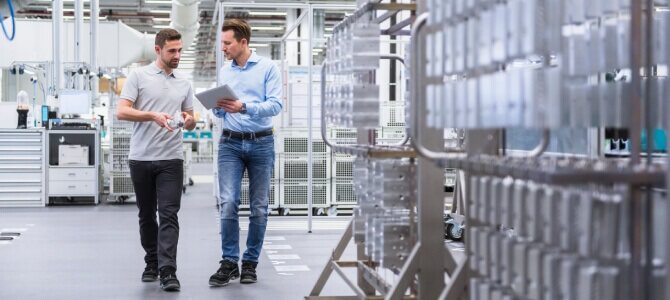 Two professionals walking through a smart manufacturing facility, using smart manufacturing software on a tablet to monitor and optimize production.