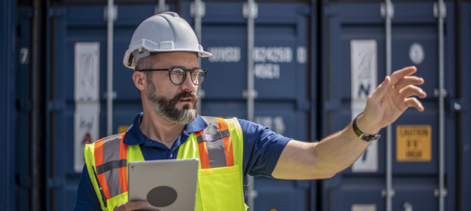 Man in front of a shipping container using a tablet to manage the global supply chain