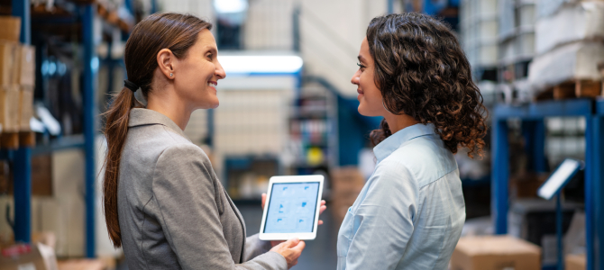 Two professionals discussing supplier performance management insights on a tablet in a warehouse setting