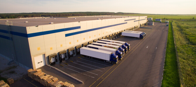 Modern distribution center with loading docks and trucks, representing global supply chain strategies such as nearshoring, reshoring, and offshoring.